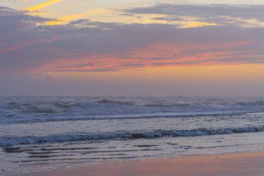 Gün batımında yumuşak okyanus dalgaları pastel renkli bir gökyüzünün altında yuvarlanır.