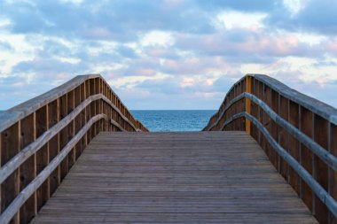 Tahta kaldırım, yumuşak bulutlarla dolu bir gökyüzünün altında, açık okyanusa doğru yavaşça kıvrılır..