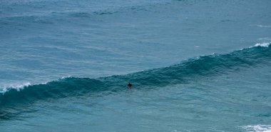 Bir sörfçünün silueti engin ve açık bir okyanusta oluşan bir dalgaya doğru kürek çeker..