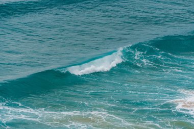 Bir turkuaz okyanus dalgası, beyaz köpükle birlikte kopmaya başlar..