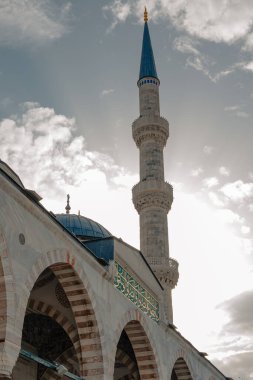 Güneş, Mavi Cami minaresinin arkasında batıyor. Mimarinin üzerine bulutlar ve gölgeler arasından çarpıcı bir ışık saçıyor..