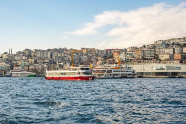 İstanbul, Türkiye, 7 Ocak 2025. Arka planda yoğun yamaç daireleri ve deniz kıyısındaki binalarla Boğaz 'dan geçen yolcu feribotları..