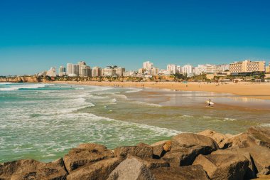 Portimao, Portekiz, 21 Şubat 2026. Praia da Rocha 'da dalgaların yanında sörf tahtası taşıyan bir sörfçü..