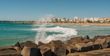 Portimao, Portekiz, 21 Şubat 2026. Güçlü Atlantik dalgaları Praia da Rocha plajı ve arka planda şehir silueti ile dalgalanan kayalık dalgalar.