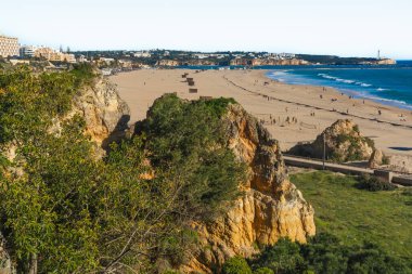 Portimao, Portekiz, 21 Şubat 2026. Praia da Rocha 'daki kayalık kayalıklardan altın kum, Atlantik dalgaları ve Algarve' deki şehir silueti.