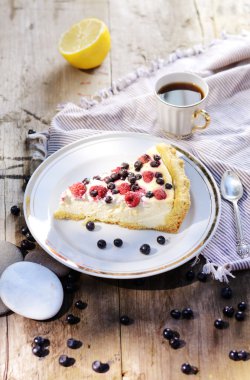 Güneşli fotoğraf rustik tarzda bir sabah kahvaltı ile. Ahşap masa üzerinde bir yaban mersini ve peynirli kek ahududu.