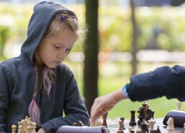 Beautiful Smart Girl, seven years old is taking part a kids chess tournament outdoor in the park.