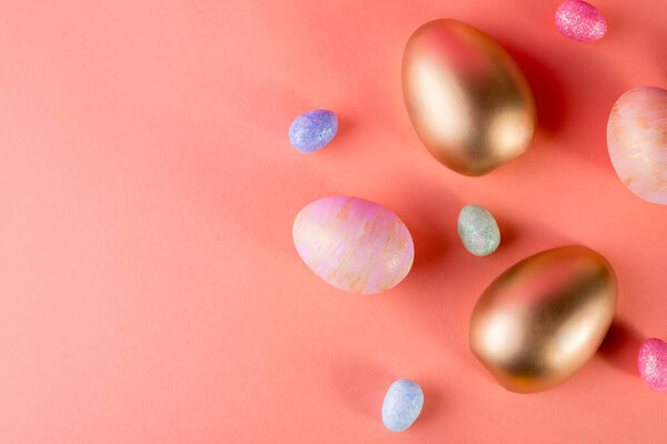 Модный пасхальный фон с золотыми и цветными пасхальными яйцами на светлом коралловом фоне с копировальным пространством для текста. Вид сверху лежал натюрморт. Пасхальная концепция.