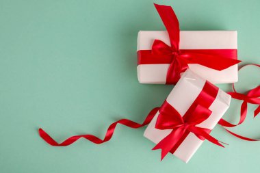 Aqua mavisi arka planda parlak kırmızı fiyonklarla bağlanmış iki beyaz hediye kutusu ve metin için boşluk. Noel ve Yeni Yıl afişleri için iyi.