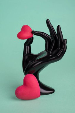 Turkuaz arka planda kırmızı kalp sembolü tutan plastik kadın eli mankenler..