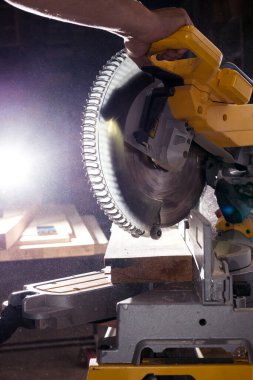 Marangoz, karanlık arka plana karşı tahta kesmek için elektrik dairesi düzenleyicisiyle çalışıyor..