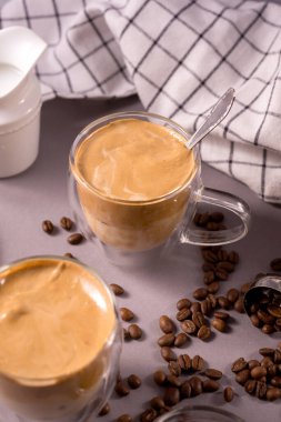 Dalgona Kahve. Kremalı içecek, hazır kahve Kore 'de popüler, şeffaf, çift cam bardakta, gri arka planda.