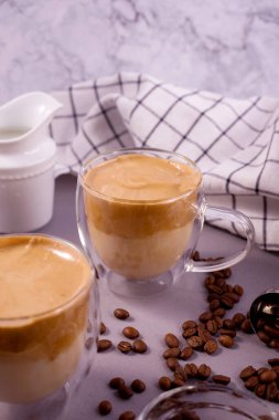 Dalgona Kahve. Kremalı içecek, hazır kahve Kore 'de popüler, şeffaf, çift cam bardakta, gri arka planda.
