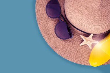 Güneş kremi spreyi şişesi ve yazlık hasır şapka plaj ayakkabıları ve mavi fotokopi alanına karşı güneş gözlüğü. Yaz tatili afişi.