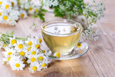 Parlak güneş ışığına karşı ahşap bir masada papatya çiçekli büyük bir fincan sıcak bitki çayı..