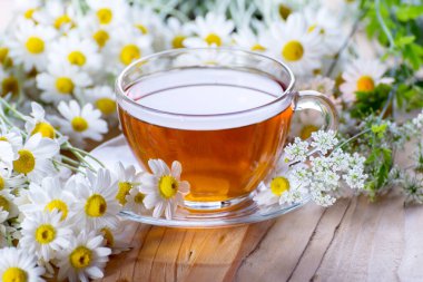 Parlak güneş ışığına karşı ahşap bir masada papatya çiçekli büyük bir fincan sıcak bitki çayı..