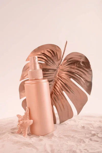 Crema protector solar o botella de loción con hoja de monstera tropical coloreada en oro rosa. Cuidado de la salud durante el concepto de vacaciones. — Foto de Stock