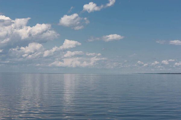 The minimalist seaside landscape and a beautiful blue sky full of fluffy clouds above that reflect in the water surface.