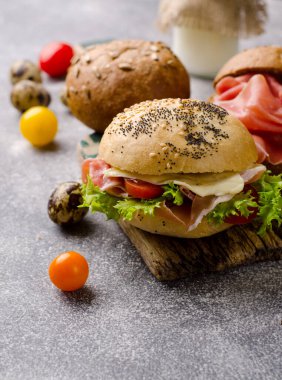 Kaliteli ahşap kesme tahtasının üzerinde dilimlenmiş jambonlu lezzetli çıtır burger ekmeği. Karanlık, karamsar yiyecekler..