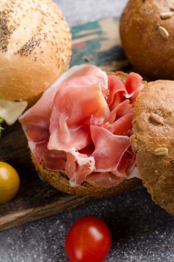 Kaliteli ahşap kesme tahtasının üzerinde dilimlenmiş jambonlu lezzetli çıtır burger ekmeği. Karanlık, karamsar yiyecekler..