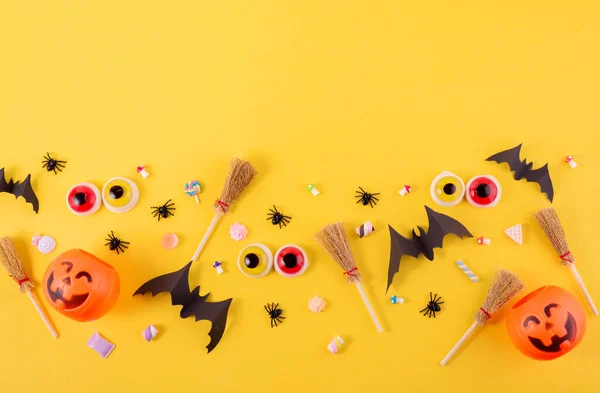 Marco de Halloween con calabazas, arañas y murciélagos recortados de papel sobre un fondo amarillo brillante. Ojos asustadizos y escobas de brujas en un concepto de Halloween de vista superior. —  Fotos de Stock