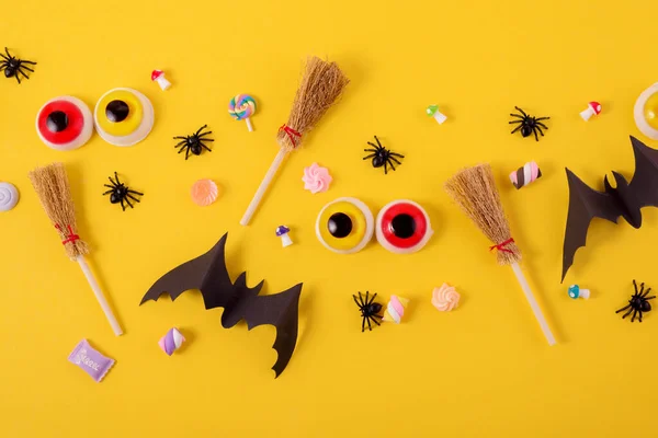 Marco de Halloween con calabazas, arañas y murciélagos recortados de papel sobre un fondo amarillo brillante. Ojos asustadizos y escobas de brujas en un concepto de Halloween de vista superior. —  Fotos de Stock