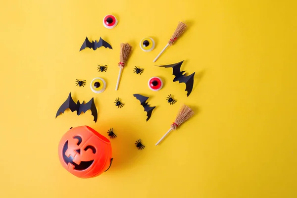 Marco de Halloween con calabazas, arañas y murciélagos recortados de papel sobre un fondo amarillo brillante. Ojos asustadizos y escobas de brujas en un concepto de Halloween de vista superior. —  Fotos de Stock