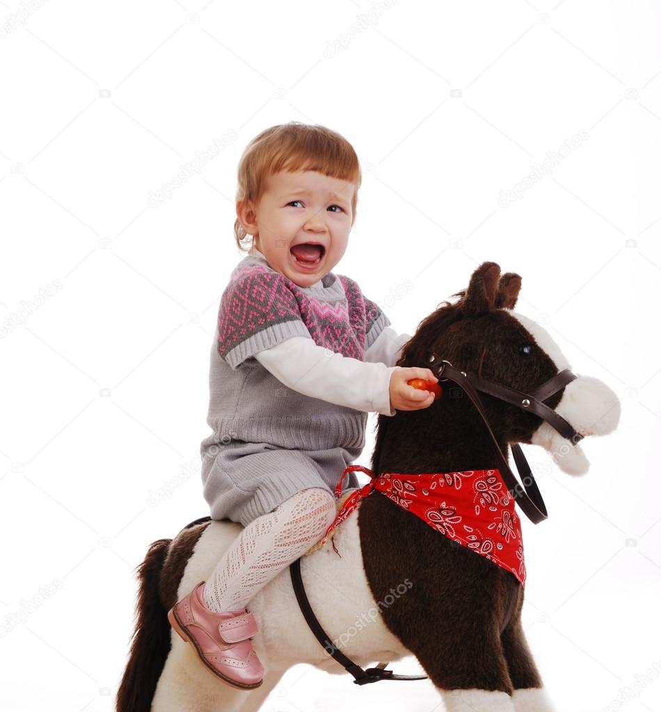 Little girl on her first toy horse isolated on a white