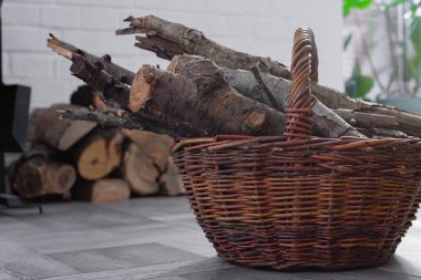 Wicker Basket, şöminenin yanında yakacak odunları olan sıcak bir ev. Arka planda istiflenmiş kütükler. Kış ısıtma kırsal yaşam tarzı konsepti.
