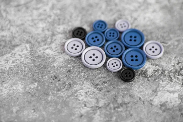 Pile of blue matte buttons on concrete background, macro bokeh. beautiful needlework. Use for sew. Space for text