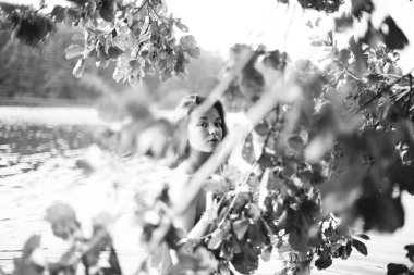 Genç, çekici, ince esmer ve mutlu bir kadının yaz yeşillikleri ve banliyö gölündeki siyah beyaz portresi.