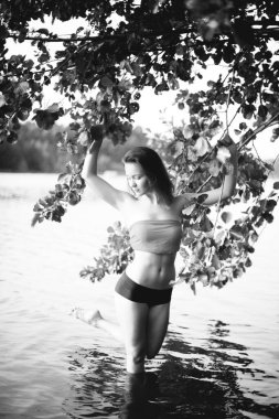 Genç, çekici, ince esmer ve mutlu bir kadının yaz yeşillikleri ve banliyö gölündeki siyah beyaz portresi.