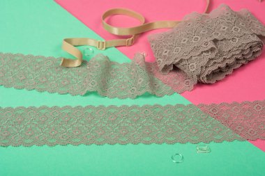 Siyah yumuşak kurdeleli bej renkli bantlar, mobilyalı dantel kumaş, aksesuarlar, bantlar, pembe ve yeşil arka planda yüzükler. Elastik malzeme. Atıcı ve nakış dükkanı için kullanılıyor.