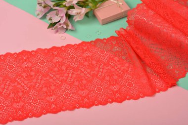 Nazik kırmızı kurdele bantları, mobilya ve çiçekli dantel kumaş, aksesuarlar, bantlar, pembe ve yeşil arka planda yüzükler. Elastik malzeme. Atıcı ve nakış dükkanı için kullanılıyor.