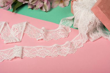 Nazik beyaz kurdele bantları, mobilya ve çiçekli dantel kumaş, aksesuarlar, bantlar, pembe ve yeşil arka planda yüzükler. Elastik malzeme. Atıcı ve nakış dükkanı için kullanılıyor.