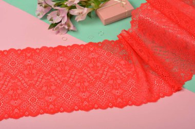 Nazik kırmızı kurdele bantları, mobilya ve çiçekli dantel kumaş, aksesuarlar, bantlar, pembe ve yeşil arka planda yüzükler. Elastik malzeme. Atıcı ve nakış dükkanı için kullanılıyor.