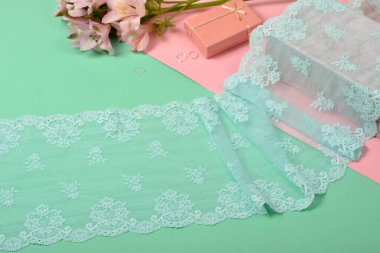 Zarif mavi kurdele, mobilya ve çiçekli dantel kumaş, aksesuarlar, bantlar, pembe ve yeşil arka planda yüzükler. Elastik malzeme. Atıcı ve nakış dükkanı için kullanılıyor.