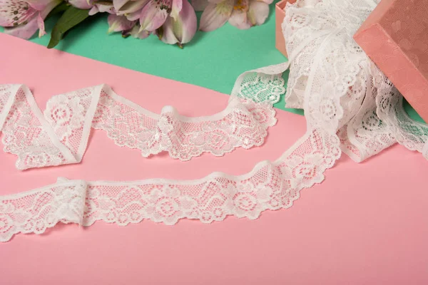 Nazik beyaz kurdele bantları, mobilya ve çiçekli dantel kumaş, aksesuarlar, bantlar, pembe ve yeşil arka planda yüzükler. Elastik malzeme. Atıcı ve nakış dükkanı için kullanılıyor.