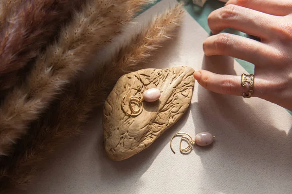 Trendy vintage cast brass ring Stylish earrings made natural pink opal stone with Golden brass fittings piece of wood pattern from activity bark beetle. And woman hand. Natural day solar lighting. — Stock Image Trendy Vintage Cast Brass Ring Stylish Earrings Made Natural Pink Royalty Free Stock Photos