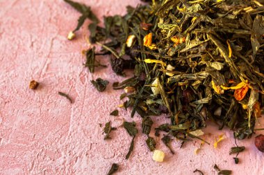 Seçkin yeşil yapraklar Sencha çayı ve şekerli meyveler, şahin üzümü, portakal kabuğu, kuru takviye yaprakları, pembe beton arka planda dondurulmuş deniz dikenleri..