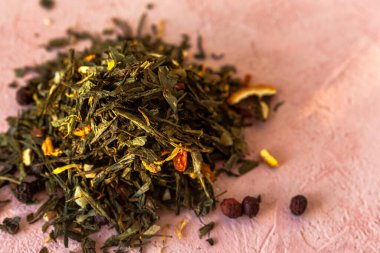Seçkin yeşil yapraklar Sencha çayı ve şekerli meyveler, şahin üzümü, portakal kabuğu, kuru takviye yaprakları, pembe beton arka planda dondurulmuş deniz dikenleri..