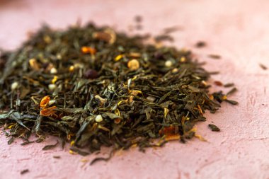 Seçkin yeşil yapraklar Sencha çayı ve şekerli meyveler, şahin üzümü, portakal kabuğu, kuru takviye yaprakları, pembe beton arka planda dondurulmuş deniz dikenleri..