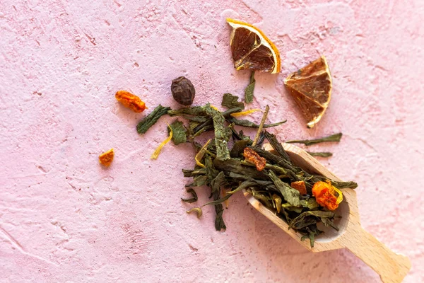 エリートグリーンの葉の山煎茶と砂糖漬けの果物 サンザシの実 オレンジの皮 乾燥したカレンデュラの花びら ピンクのコンクリートの背景に凍結乾燥した海のクロウメモドキ — ストック写真