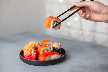Çeşitli türlerde somon suşi rulosu servis edilir, servis edilir. Geleneksel Asya yemekleri betonun üzerinde siyah tabakta. Seçici yumuşak odağı kapat.