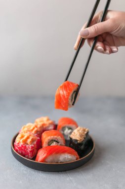 Çeşitli türlerde somon suşi rulosu servis edilir, servis edilir. Geleneksel Asya yemekleri betonun üzerinde siyah tabakta. Seçici yumuşak odağı kapat.