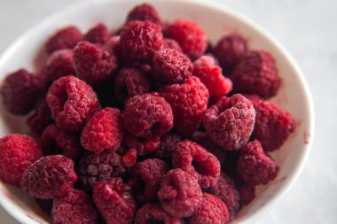 Donmuş taze taze taze, beyaz tabakta kırmızı ahududu yığını. Yaz meyveli vejetaryen konsepti. Seçici yumuşak odak yakın plan.