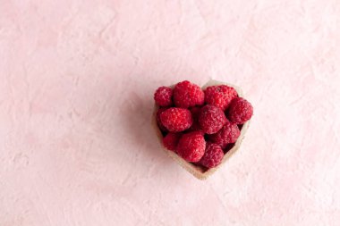 Pembe betonun üzerinde taze donmuş, olgun, parlak kırmızı ahududu yığını. Yaz meyveli vejetaryen konsepti. Seçici yumuşak odak.