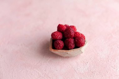 Pembe betonun üzerinde taze donmuş, olgun, parlak kırmızı ahududu yığını. Yaz meyveli vejetaryen konsepti. Seçici yumuşak odak.