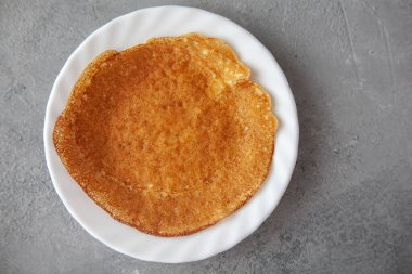 Lezzetli kızarmış ince krepler beyaz tabakta gri beton arka planda, karnaval shrove günü, soya karbonhidratsız protein ketojenik fırın ürünleri.