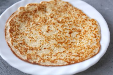 Lezzetli kızarmış ince krepler beyaz tabakta gri beton arka planda, karnaval shrove günü, soya karbonhidratsız protein ketojenik fırın ürünleri.